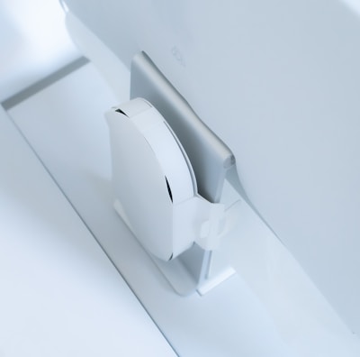 A white, sleek, vertical gaming console placed beside a large, slim monitor. The setting exudes minimalism with a focus on modern technology design.