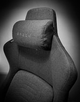 A high-quality, fabric gaming chair featuring ergonomic design and enhanced comfort. The chair has a distinct headrest with visible stitching, embossed branding, and a modern aesthetic.